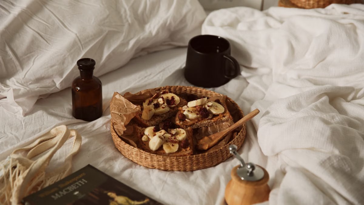 A cozy breakfast in bed setup featuring banana toast and a cup of coffee on a wicker tray, creating a warm and inviting scene.